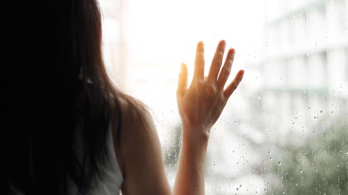 A woman forlornly looking out a window.
