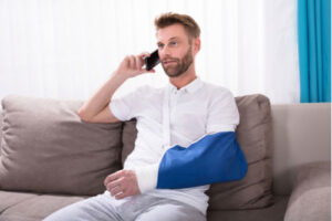 Man with arm in cast and sling calling Charlotte rear-end car accident lawyer on mobile phone