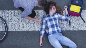 A man checking on a woman who has been hit by a car lying on the road