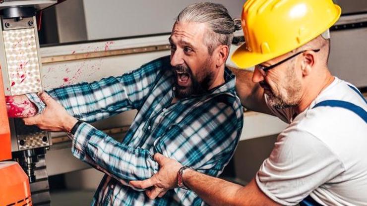 A man helping a coworker who has their arm stuck in machinery.