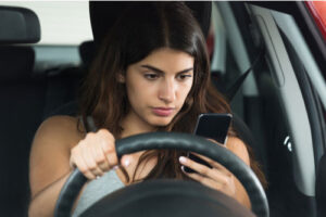 Young woman looking at her mobile phone while driving